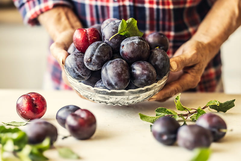 Close-up on a dish full of fresh plums being held over a kitchen counter